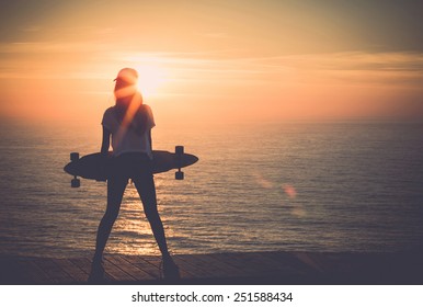 Beautiful girl holding a skateboard with the sunset in the background - Powered by Shutterstock