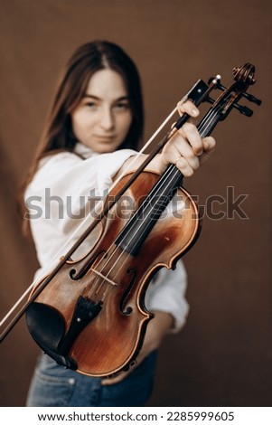 Beautiful girl holds violin in her hands. Violinist in white shirt and jeans