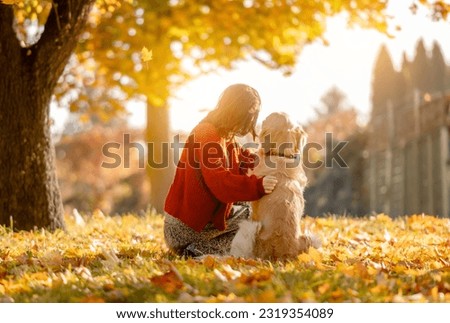 Beautiful girl hugging golden retriever dog in autumn park sitting in yellow leaves and looking at sun. Pretty young woman with purebred doggy labrador at fall season at nature