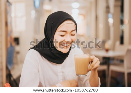 Beautiful girl laughing while drinking hot tea with milk,known as Teh Tarik with bokeh background and retro filter effect.