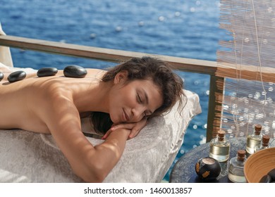 Beautiful girl laying down on a massage bad with zen stones on her relaxing near sea front spa area - Shutterstock ID 1460013857
