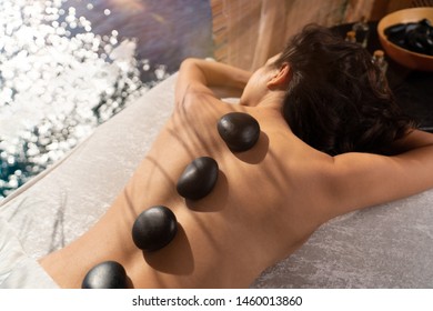 Beautiful girl laying down on a massage bad with zen stones on her relaxing near sea front spa area - Shutterstock ID 1460013860