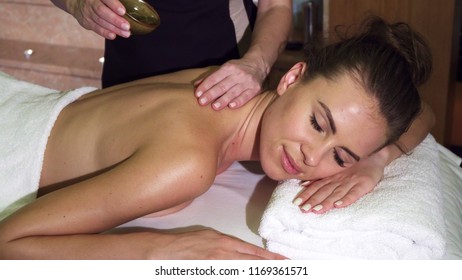 A beautiful girl lies on a massage table. She came to the spa salon and for treatment. Masseuse watering the girl with oil. She is given an exquisite massage