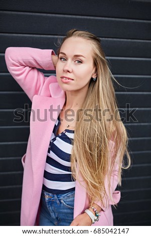 A beautiful girl with long blond hair in a pink coat walks the streets of the city 