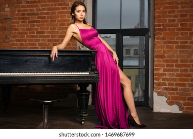 Beautiful girl in long classic red dress posing with old piano. - image