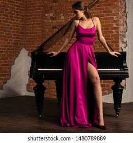 Beautiful girl in long classic red dress posing with old piano. 