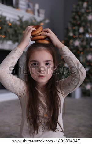 Beautiful girl with long dark hair is fooling around with cookies on New Year's bokeh lights at a decorated Christmas tree