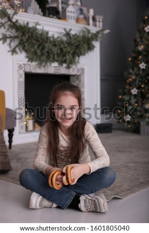 Beautiful girl with long dark hair is fooling around with cookies on New Year's bokeh lights at a decorated Christmas tree