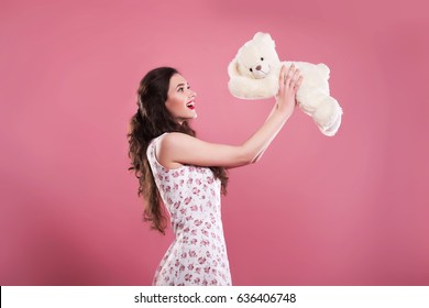 Beautiful girl with long hair holds a toy bear on a pink background
