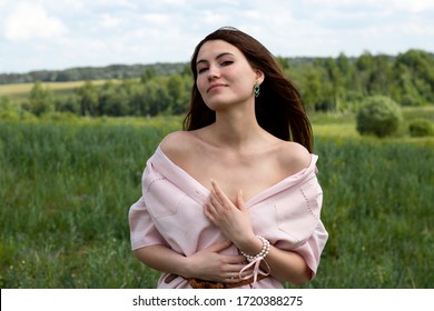 Beautiful girl with long hair, off the shoulder in a pink linen dress in nature. Cute, romantic girl on the field. Portrait of a girl on a field background.