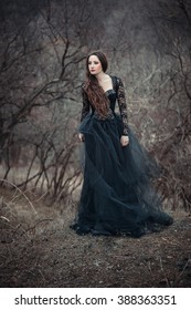 Beautiful girl with long hair standing in a black dress standing on the gothic background blowers forests, forest princess, halloween , dark boho , fashionable toning , creative color
