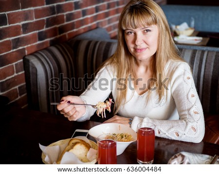 Beautiful girl with long hair and a white knitted sweater eats a salad in a cafe
