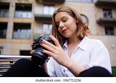 A beautiful girl looks in the viewfinder in the camera, and takes pictures. The blonde learns to photograph and earn money on the photo. A girl photographer walks around the city and takes pictures 