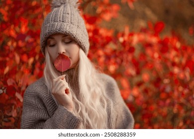 A beautiful girl with loose long blond hair walks in the fall park and admires the views of the red autumb park atmosphere. The woman is wearing jeans,  a sweater and knitted biege hat - Powered by Shutterstock