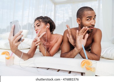 Beautiful girl making selfie with smartphone and showing v sign with handsome african man at the beach