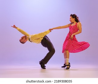 Beautiful Girl And Man In Colorful Retro Style Costumes Dancing Incendiary Dances Isolated On Lilac Color Background In Neon Light. Actors In Motion And Action. Concept Of Art, 60s, 70s Culture