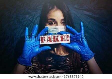 Beautiful girl in a medical mask and blue protective rubber gloves. A young woman holds a red inscription "Fake" on a dark blue background.