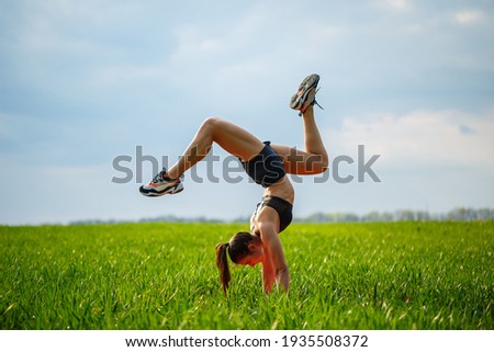 beautiful girl model on green grass do yoga. A beautiful young woman on a green lawn performs acrobatic elements. flexible gymnast in black does a handstand in split