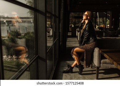 beautiful girl model in a restaurant in a beautiful loft interior. on the eyes of sunglasses, dressed in a leather black jacket, casual clothes. warm photography, sunlight
