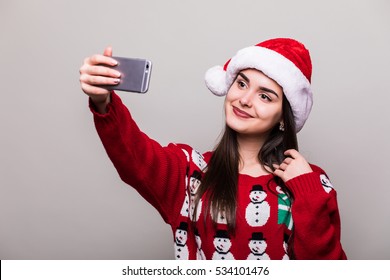 Beautiful Girl Model Wear Santa Hat And Christmas Sweater Take Selfie On Grey Background