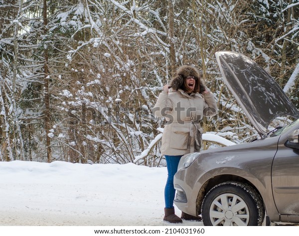 beautiful girl near the engine of a\
broken car on a winter snowy road. froze and calls for\
help
