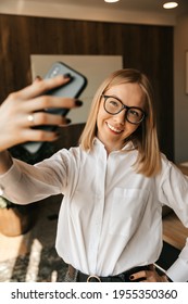 A Beautiful Girl In The Office Makes A Selfie On The Phone, A Photo On A Smartphone At Work. High Quality Photo