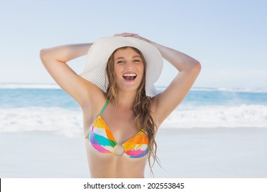 Beautiful girl on the beach smiling in white straw hat and bikini on a sunny day