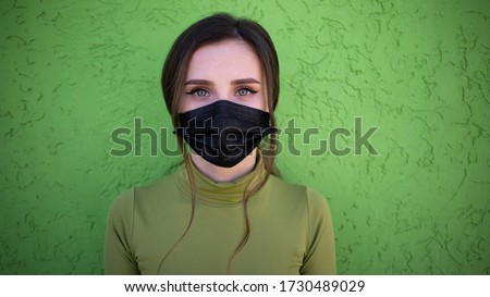 Beautiful girl on the green background with flu medical face mask. Protected and saved from respiratory problems. Black Facemask dressed. 