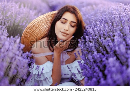 Beautiful girl on the lavender field. Portrait a woman with closed eyes inspiring the aroma of lavender flowers in white dress and straw hat the lavender field on sunset. Soft focus.Violet,purple lave