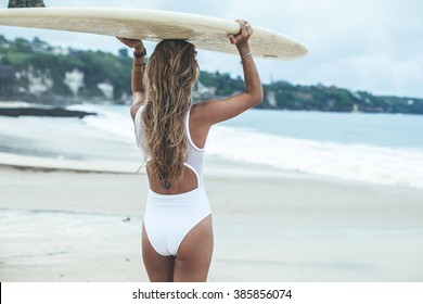 Beautiful girl on a surf board in the ocean. Girl with long hair in a white bathing suit in the ocean on the longboard. beautiful girl with a tattoo on his back in the ocean surf.