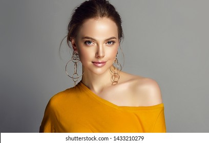 Beautiful Girl In Orange Blouse On One Shoulder . Fashionable And Stylish Women's Clothing . Fashion Look  , Beauty And Style. Young Woman In Trendy Jewelry Earrings Rings.
