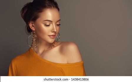 Beautiful Girl In Orange Blouse On One Shoulder . Fashionable And Stylish Women's Clothing . Fashion Look  , Beauty And Style. Young Woman In Trendy Jewelry Earrings Rings.

