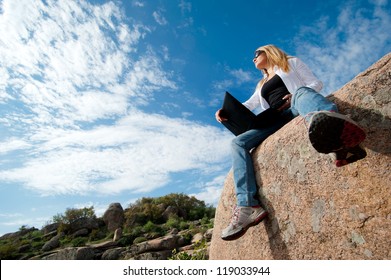 Beautiful girl outdoors with a laptop sitting on a rock