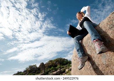 Beautiful girl outdoors with a laptop sitting on a rock