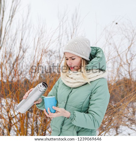 A beautiful girl outdoors pours tea from a thermos into a cup. Portrait of a girl with a cup of tea in winter, close-up.
