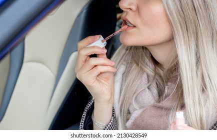 Beautiful Girl Is Painting Her Lips Sitting In A Car And Looking In The Car Vanity Mirror. Blonde Hair Color. Woman Driver.  Sun Visor Mirror Clip On. Beauty And Driving Car Concept.