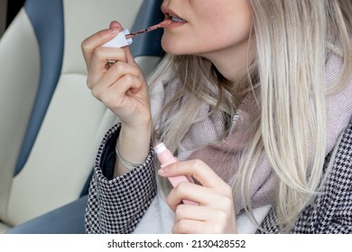 Beautiful Girl Is Painting Her Lips Sitting In A Car And Looking In The Car Vanity Mirror. Blonde Hair Color. Woman Driver.  Sun Visor Mirror Clip On. Beauty And Driving Car Concept.