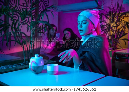 Beautiful girl with a pearl earring taking lunch in modern cafe, restaurant in neon light