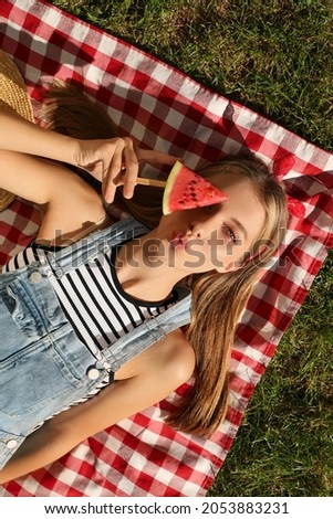 Beautiful girl with piece of watermelon on picnic blanket outdoors, top view