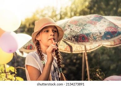 Beautiful Girl With Pigtails In Straw Hat Eating Carrot Sticks Outdoors In Hot Summer Day With Sunlight On Background