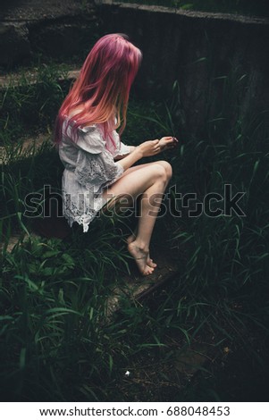 The beautiful girl with pink hair sits on the thrown ladder in an environment of a green grass