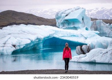A beautiful girl in a pink jacket with a massive massive iceberg in the background on the famous Jökulsárlón glacier lagoon in southern Iceland, Europe	 - Shutterstock ID 2343040519