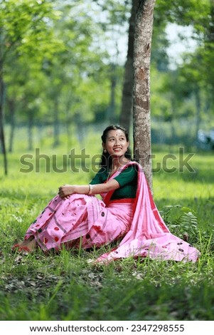 a beautiful girl in a pink sari sitting under a tree,a beautiful assamese girl in a pink makhala sador sitting under a tree