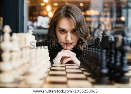 Beautiful girl play chess, queen gambit play and everyone wins, a smart and pensive face. White and black chess pieces are displayed on the board. Mental game, a lot of time to last, not for fools