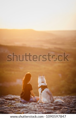 Beautiful girl plays with a dog, grey and white husky, in the mountains at sunset. Indian girl and her wolf