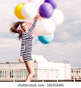 Beautiful Girl With Ponytail Hair In Short Black And White Striped Dress And White High Sneakers Jumps Holding Bunch Of Multicolored Balloons