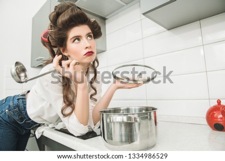 Beautiful girl is posing in everyday clothes with curlers in her hair and holding a pot. Fashion home shot. Pin-up style.