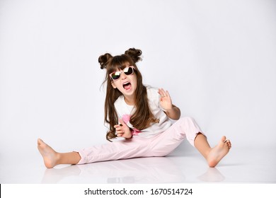 Beautiful Girl Posing Sitting On The Floor In Sunglasses, Summer Clothes And Fashionable Hairstyle, In The Studio, Screaming With Joy Legs Stretched Out In Different Directions