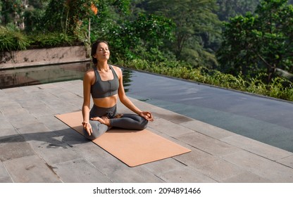 
A beautiful girl practices yoga by the pool in the morning in Bali, Indonesia. Young woman in sportswear near the infinity pool against the backdrop of a tropical landscape. - Powered by Shutterstock