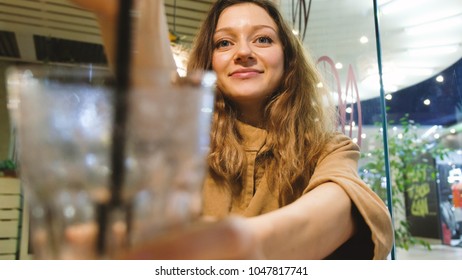 Beautiful girl proposes to drink smoothies from a straw in a cafe - Shutterstock ID 1047817741